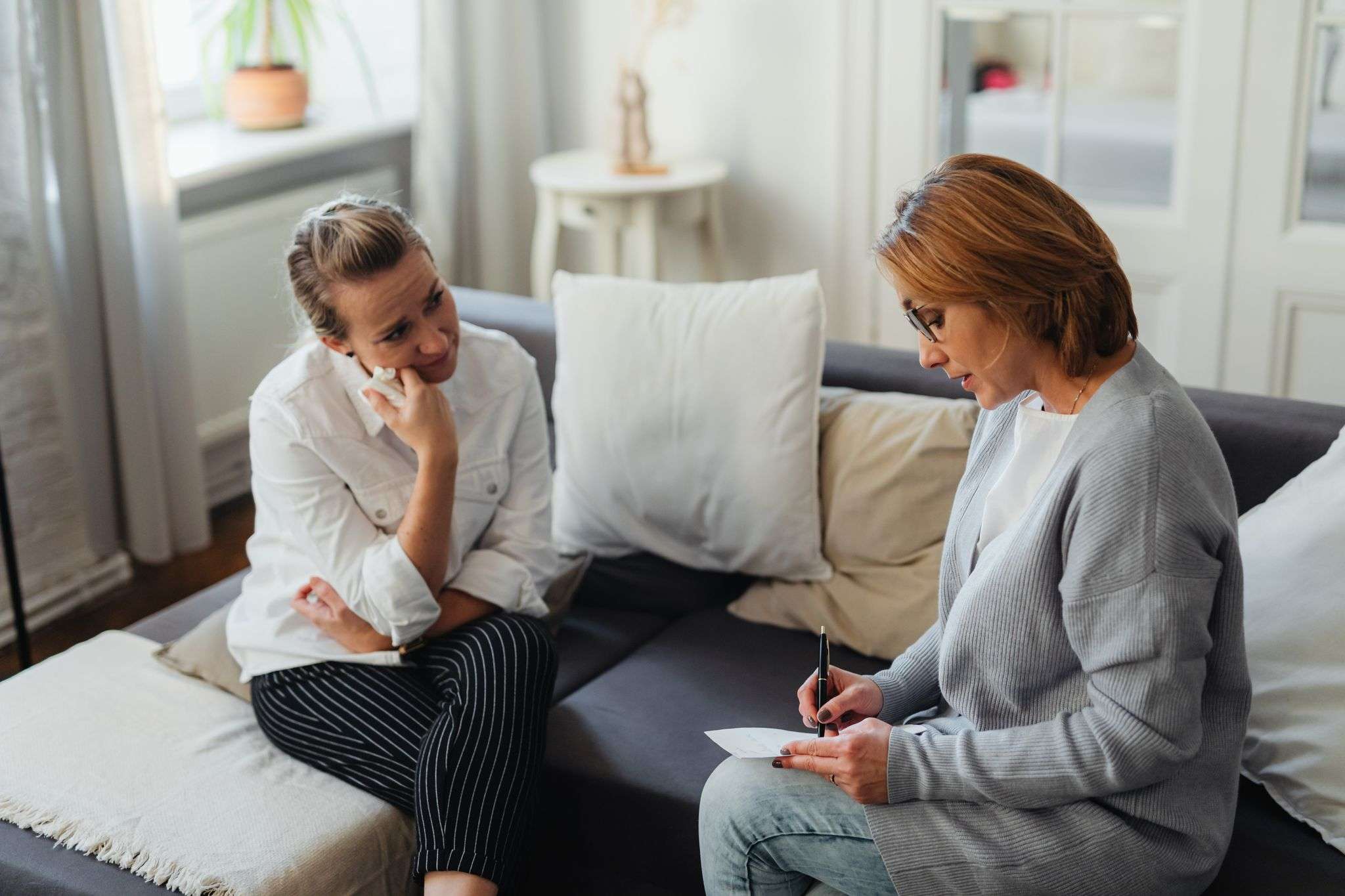 A thoughtful therapy session between two women in a cozy room.