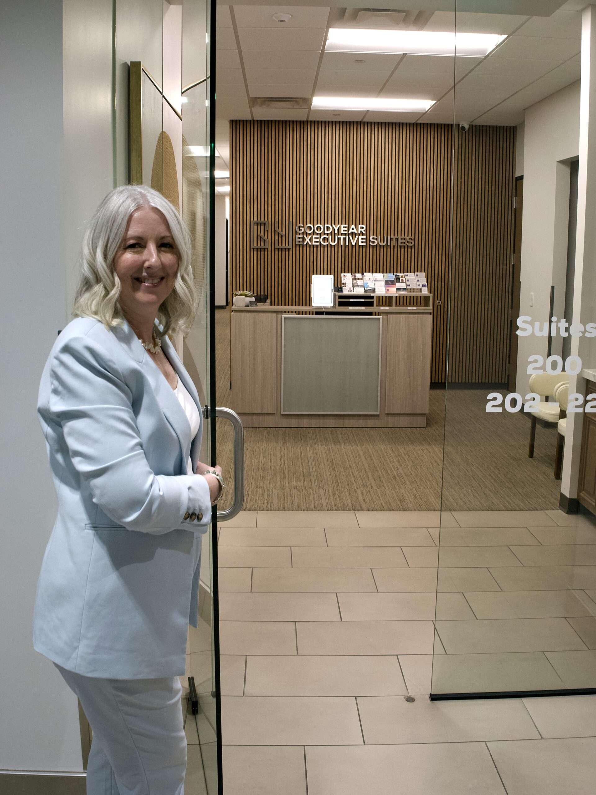 EMDR therapist welcomes clients in light blue suit holding open the door to Goodyear Suites in Arizona